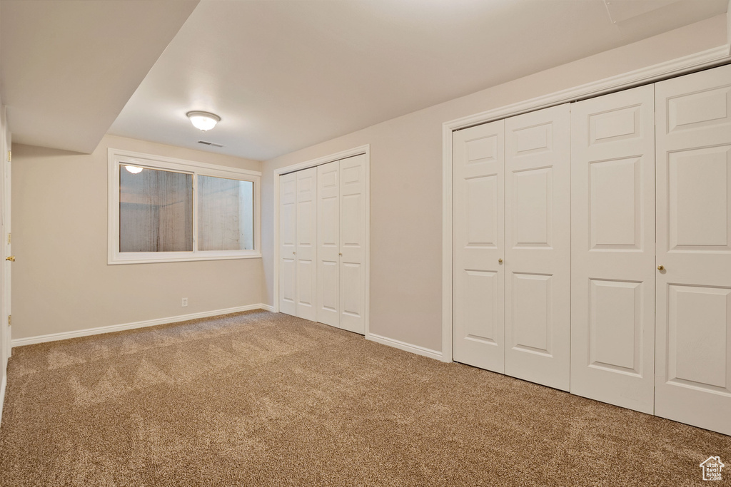 Unfurnished bedroom with carpet floors, two closets, and baseboards