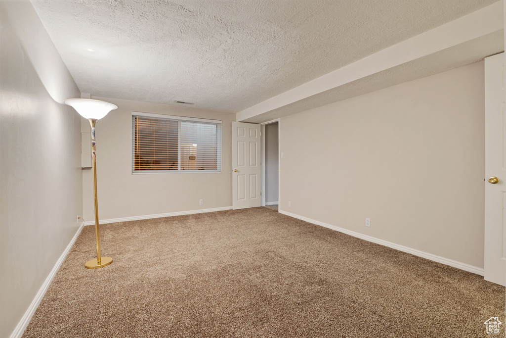 Carpeted empty room with a textured ceiling and baseboards