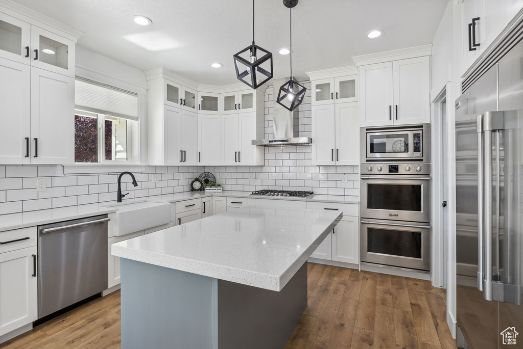 Kitchen with appliances with stainless steel finishes, a sink, decorative backsplash, light wood-type flooring, and a center island