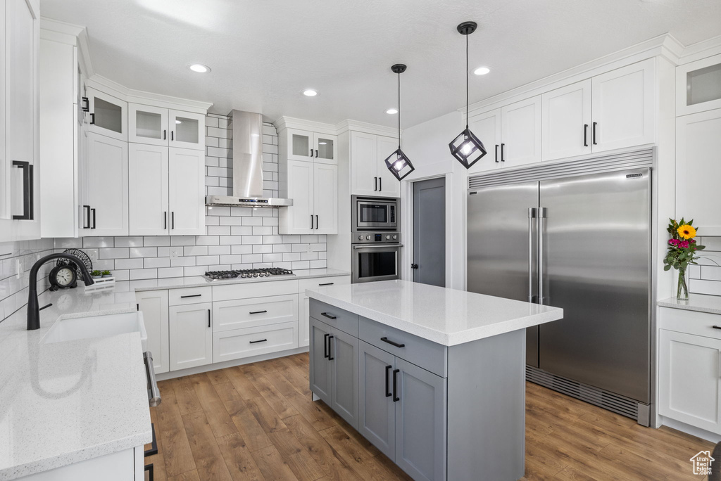 Kitchen with built in appliances, wall chimney exhaust hood, gray cabinets, a sink, and white cabinets