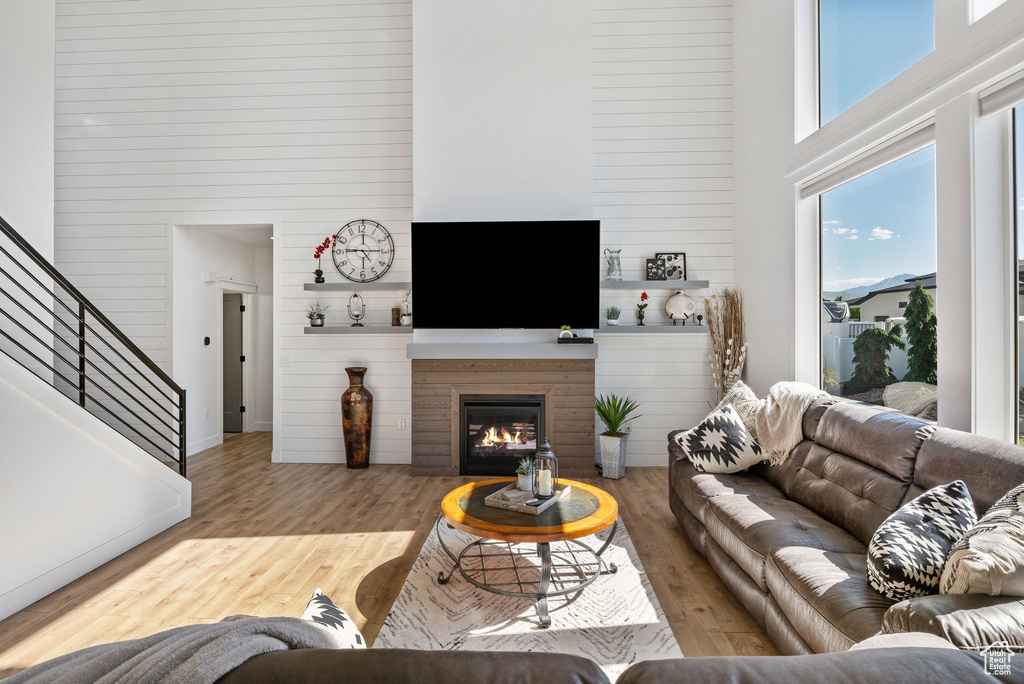Living area with a towering ceiling, a lit fireplace, stairway, wood finished floors, and wood walls
