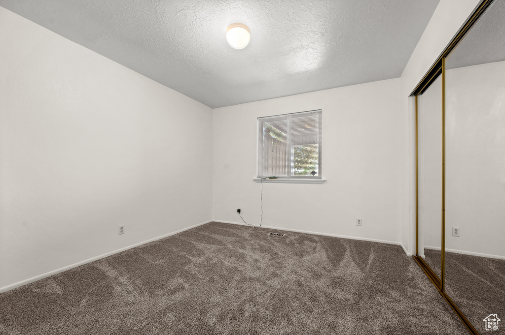 Unfurnished bedroom featuring carpet floors, a textured ceiling, a closet, and baseboards