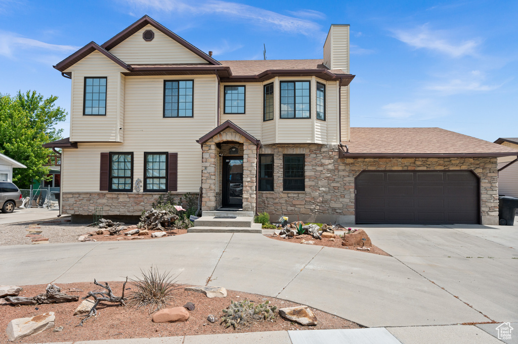 View of front of property with stone siding, an attached garage, concrete driveway, a chimney, and roof with shingles