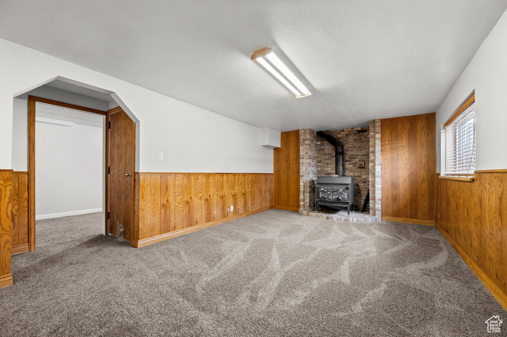 Unfurnished living room featuring wood walls, a wood stove, wainscoting, and carpet floors