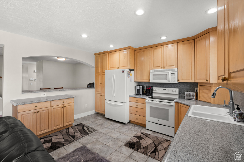 Kitchen with white appliances, a sink, arched walkways, light tile patterned flooring, and light brown cabinetry