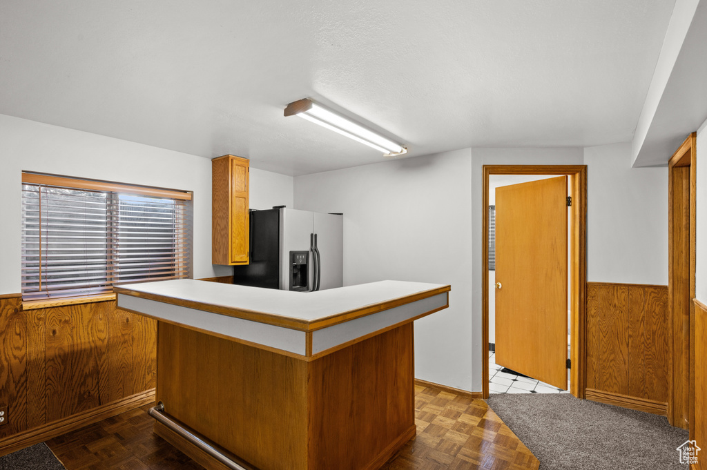 Kitchen with stainless steel fridge, wainscoting, a peninsula, wooden walls, and brown cabinetry