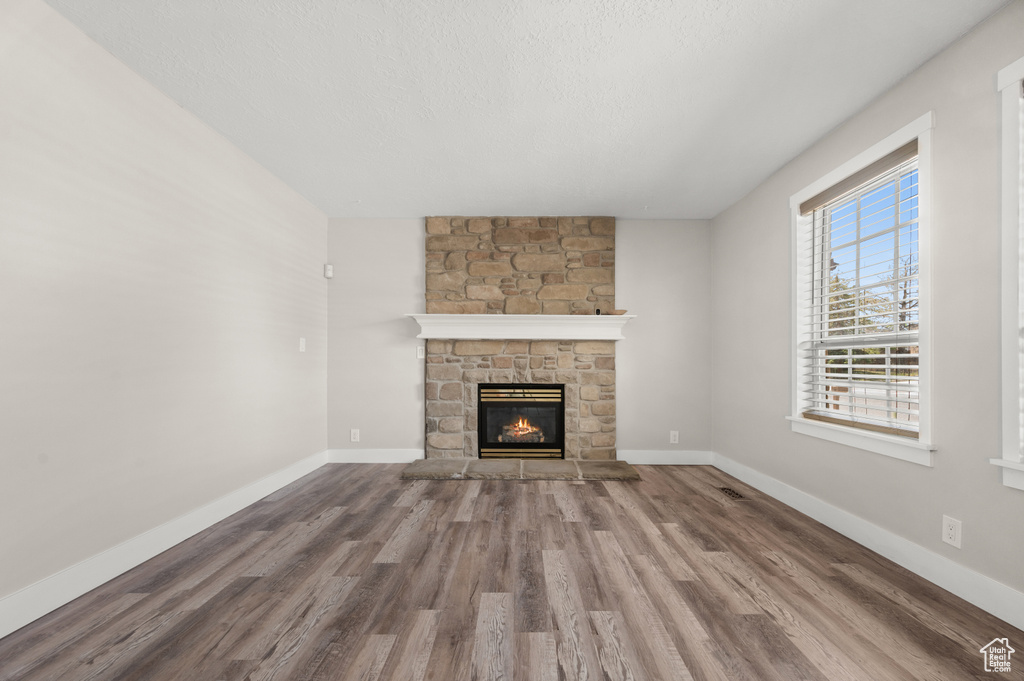 Unfurnished living room featuring wood finished floors, a stone fireplace, and baseboards