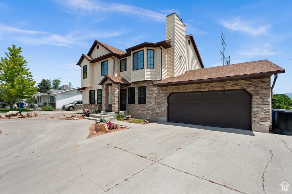 View of front of house featuring concrete driveway, stone siding, a garage, a chimney, and a shingled roof