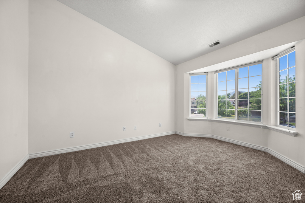 Carpeted spare room featuring vaulted ceiling and baseboards
