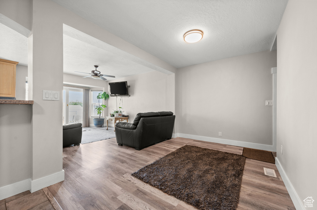 Living area featuring a ceiling fan, wood finished floors, baseboards, and a textured ceiling