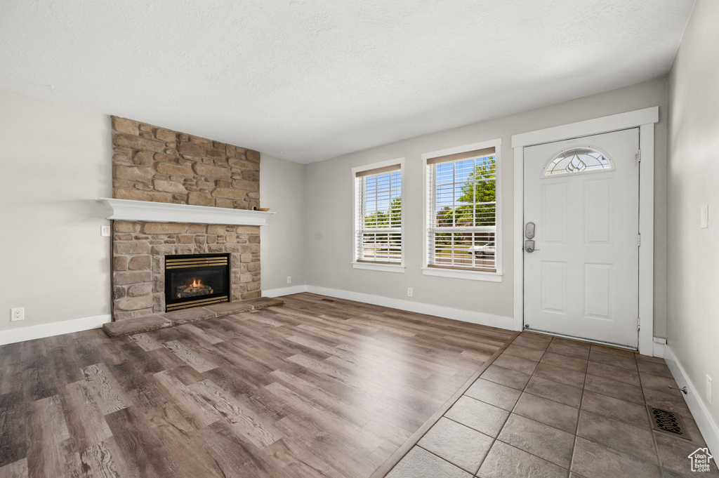 Unfurnished living room featuring a fireplace, wood finished floors, baseboards, and a textured ceiling