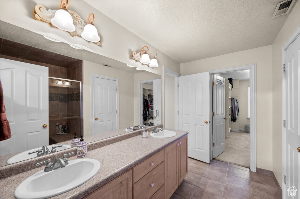 Bathroom with double vanity, a stall shower, a textured ceiling, tile patterned flooring, and a walk in closet
