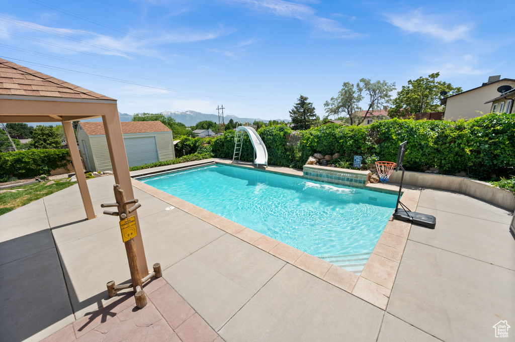 View of swimming pool with a water slide, a patio, a mountain view, and an outdoor structure