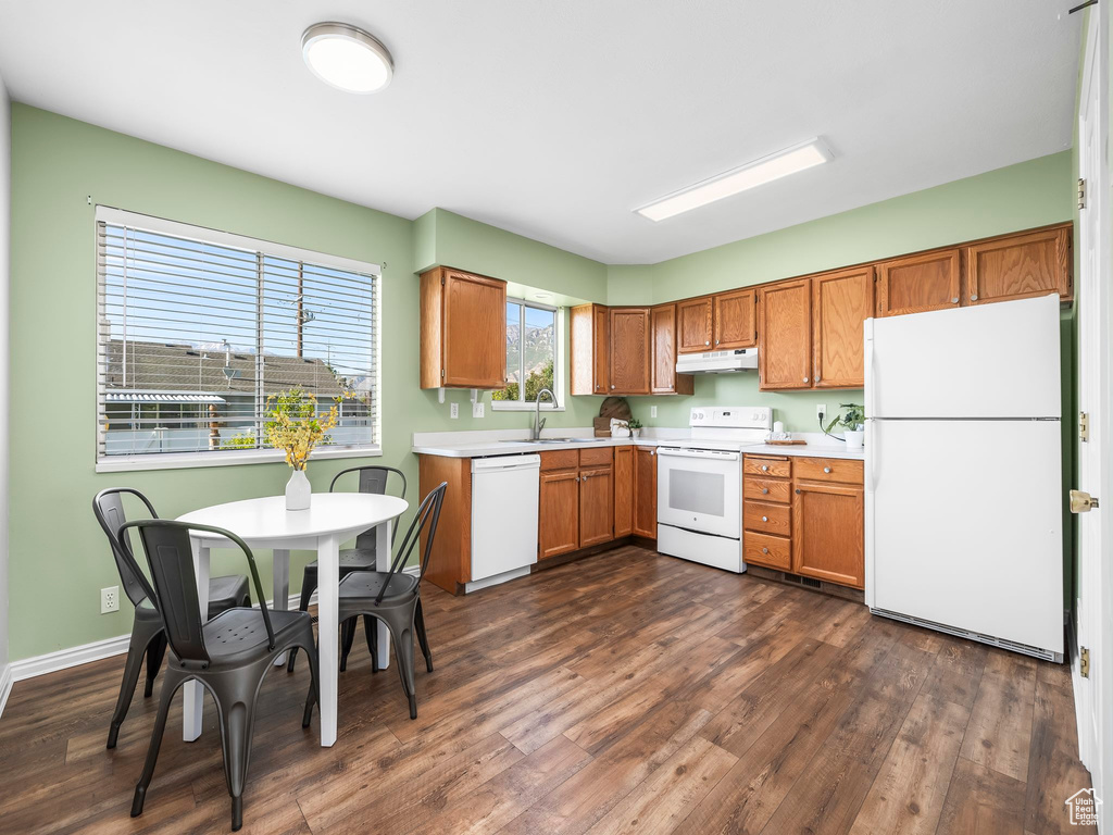 Kitchen featuring white appliances, under cabinet range hood, light countertops, dark wood finished floors, and a sink