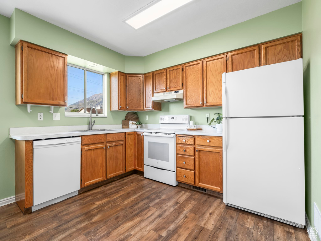 Kitchen featuring white appliances, a sink, under cabinet range hood, dark wood-style flooring, and light countertops