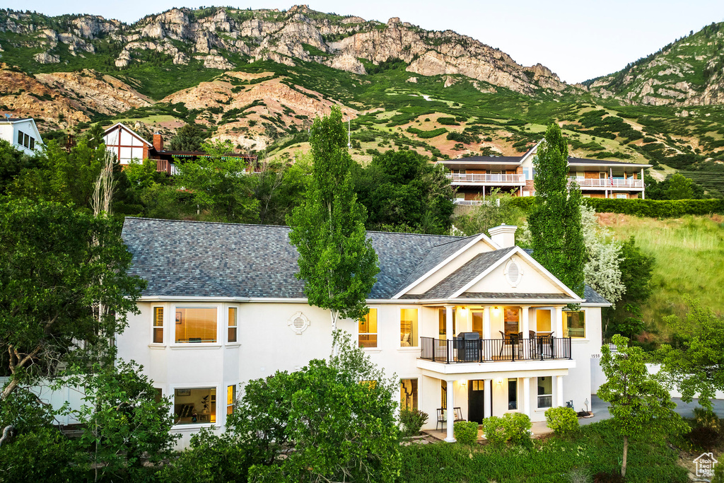 Back of property with a balcony, stucco siding, a mountain view, a chimney, and a shingled roof