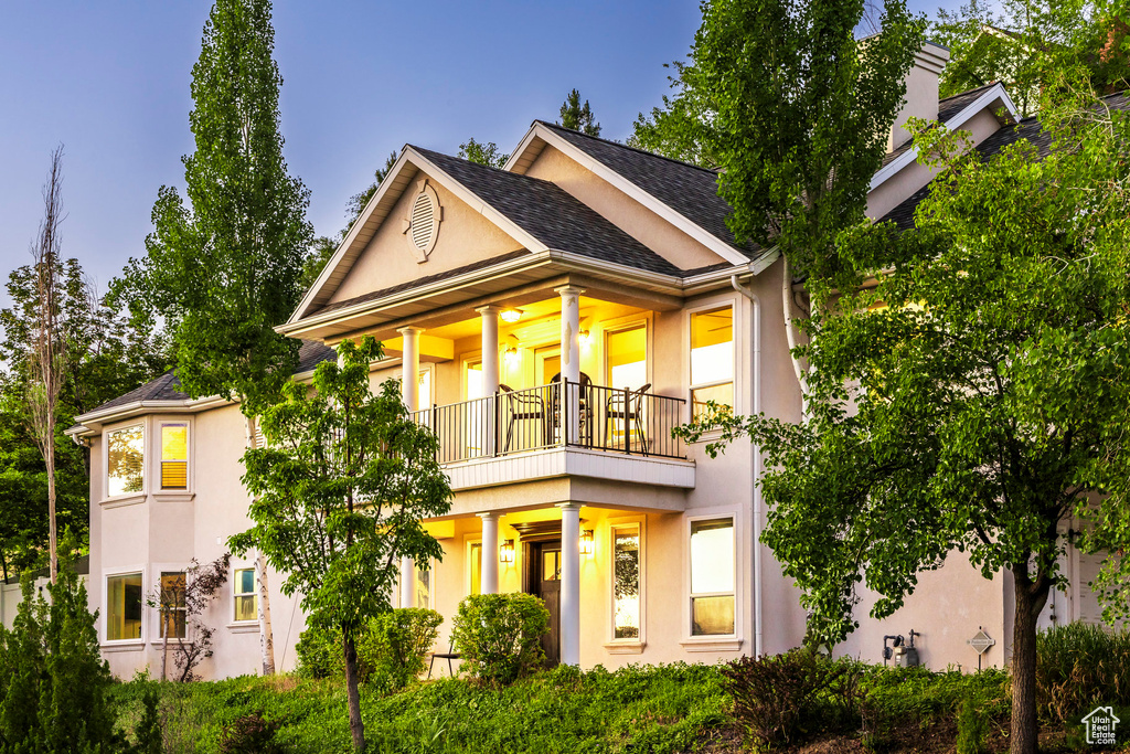 View of front of home with a balcony, stucco siding, and roof with shingles