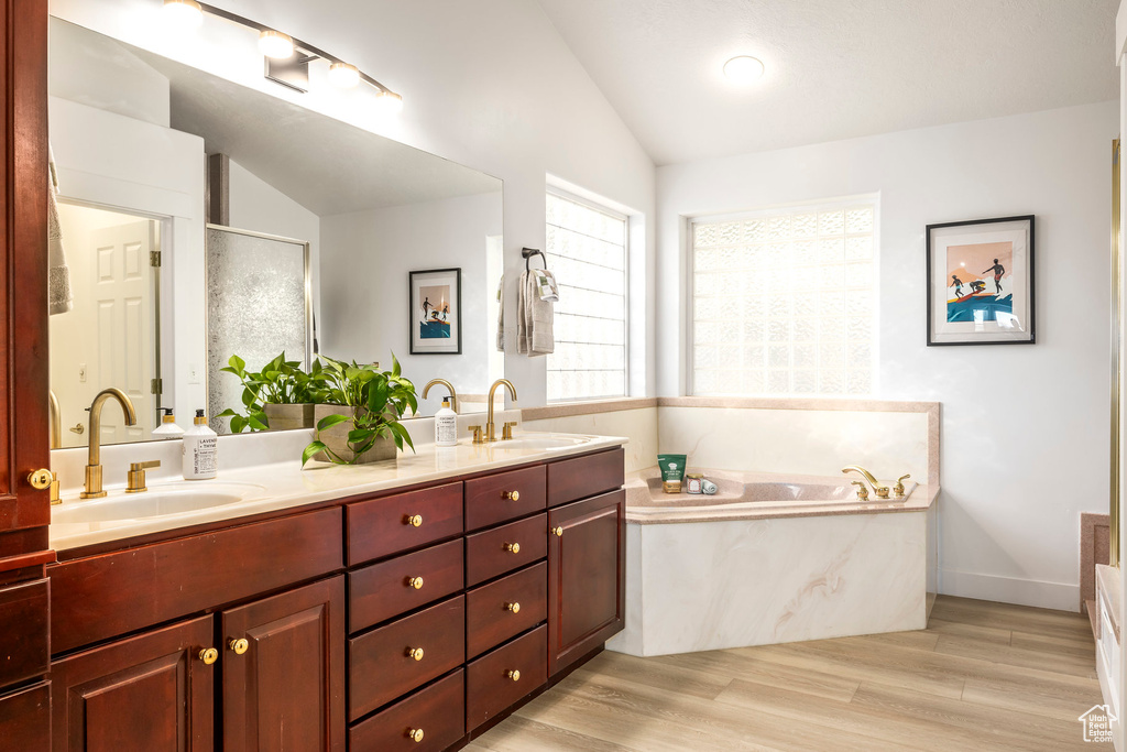 Full bathroom with vaulted ceiling, a garden tub, double vanity, a stall shower, and wood finished floors