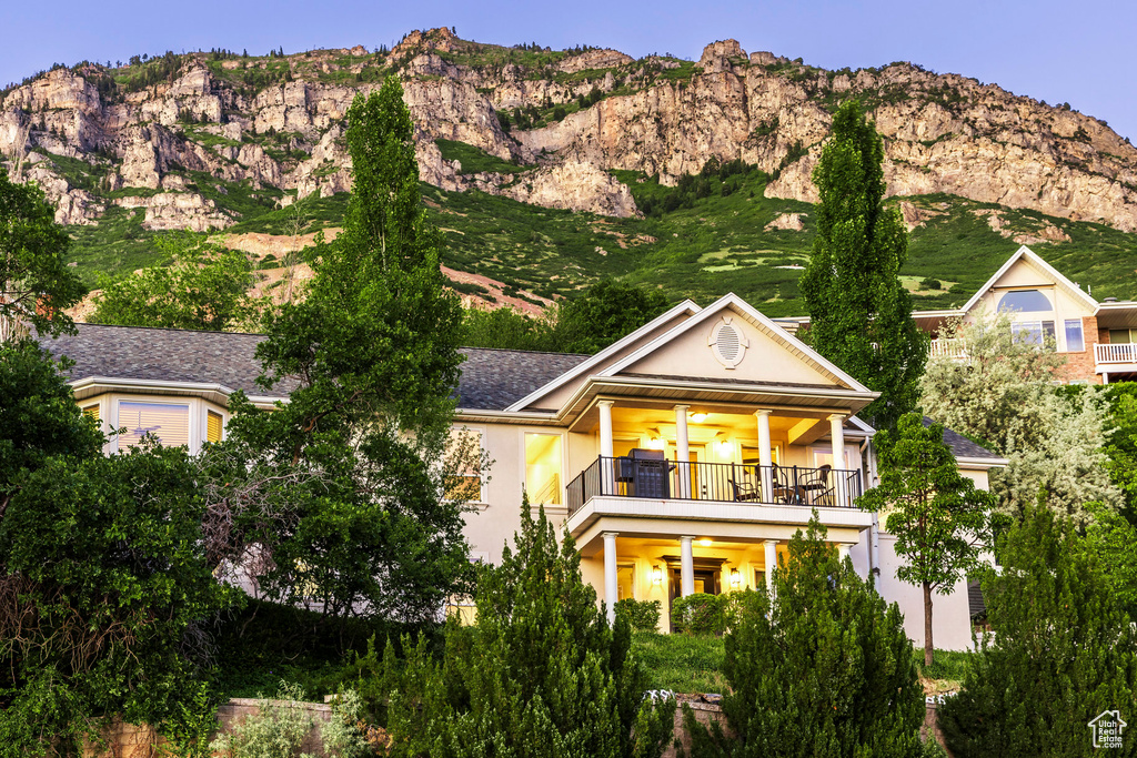 Rear view of house featuring a mountain view, stucco siding, a balcony, and ceiling fan