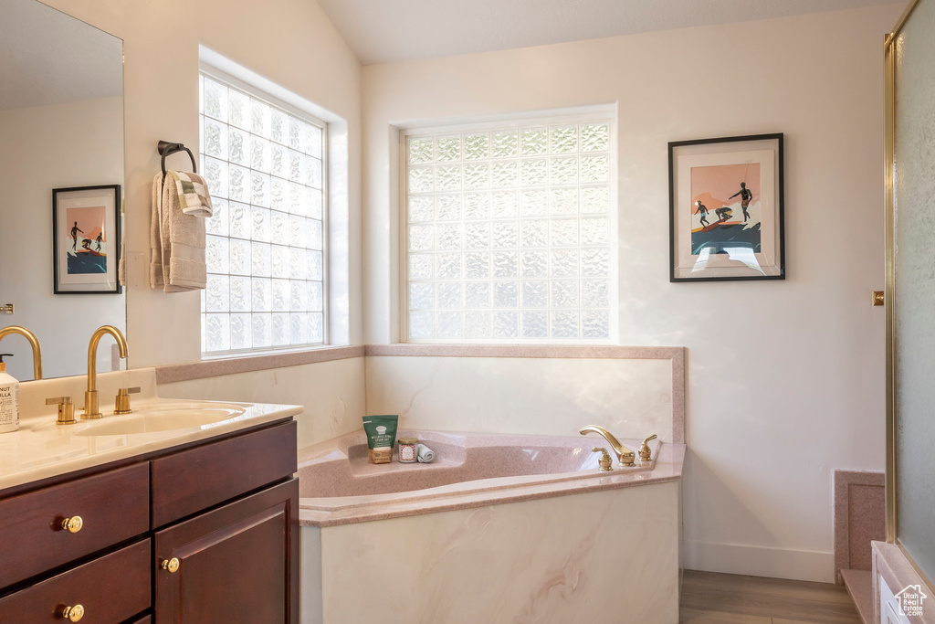Bathroom featuring vanity, a garden tub, wood finished floors, and baseboards