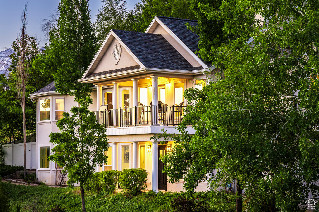 View of front of house featuring a balcony, stucco siding, and a shingled roof