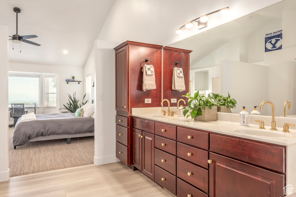 Ensuite bathroom featuring vaulted ceiling, double vanity, a ceiling fan, and wood finished floors