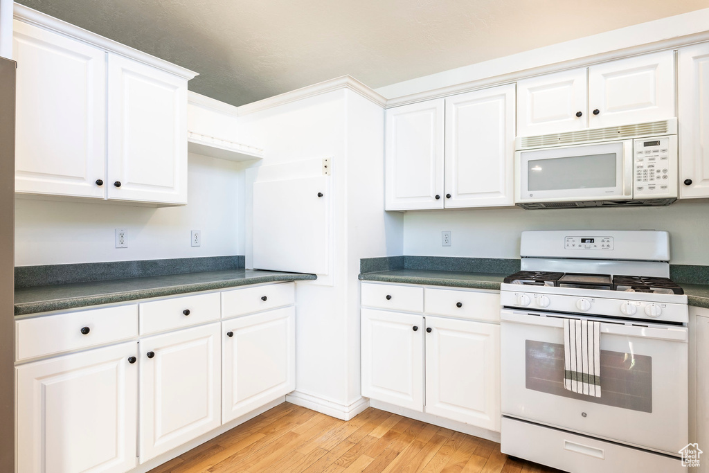 Kitchen featuring white appliances, dark countertops, light wood finished floors, and white cabinets
