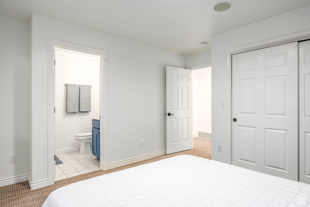 Bedroom with baseboards, a closet, ensuite bathroom, and light carpet