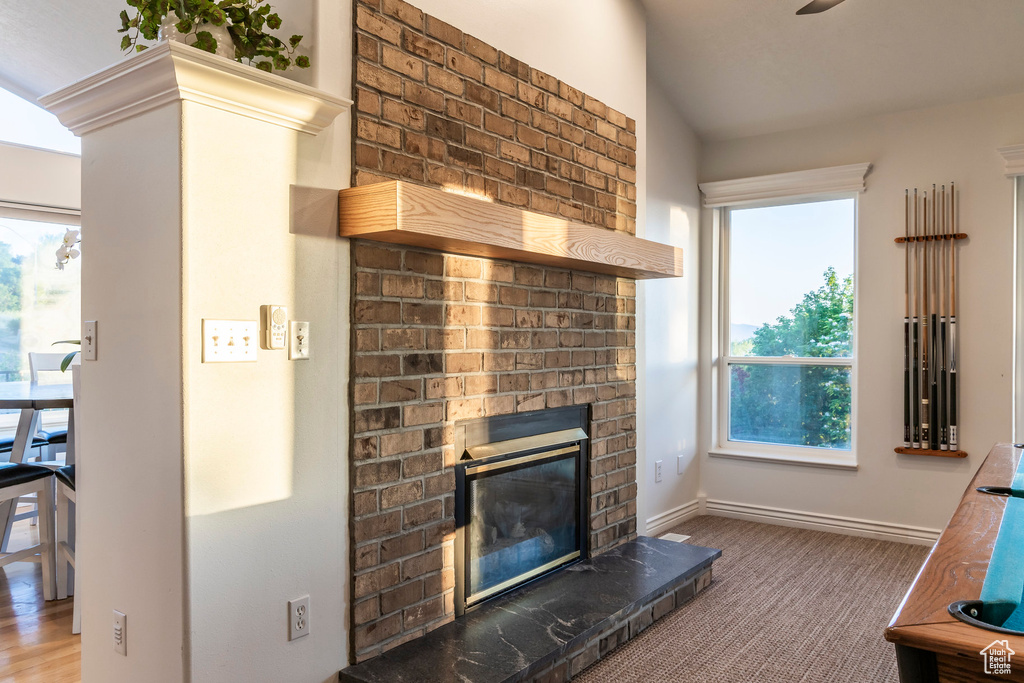 Carpeted living area featuring a brick fireplace, baseboards, and ceiling fan