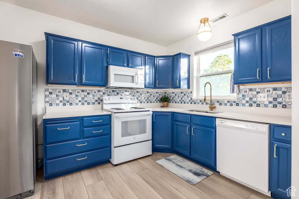 Kitchen with white appliances, blue cabinets, a sink, and light wood finished floors