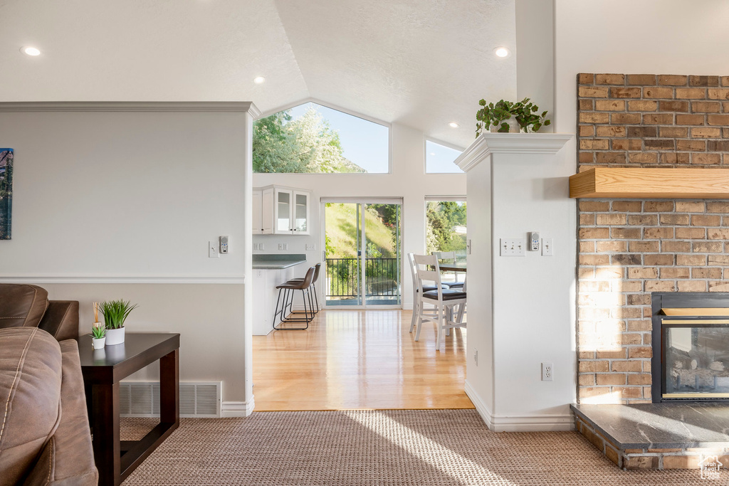 Carpeted living area with a brick fireplace, lofted ceiling, baseboards, recessed lighting, and wood finished floors