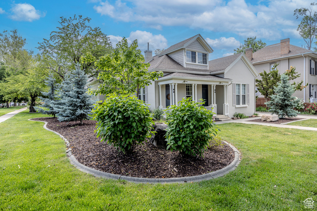 View of front of property featuring a front lawn, a chimney, stucco siding, and a porch