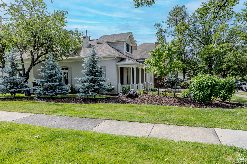 View of front of home featuring stucco siding, a front lawn, roof with shingles, and a chimney