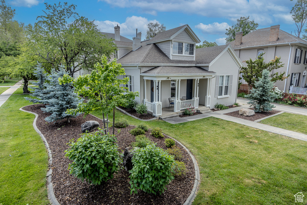 View of front of home featuring roof with shingles, covered porch, stucco siding, and a front yard
