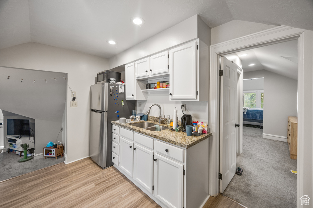 Kitchen with lofted ceiling, a sink, appliances with stainless steel finishes, white cabinets, and light wood-style flooring