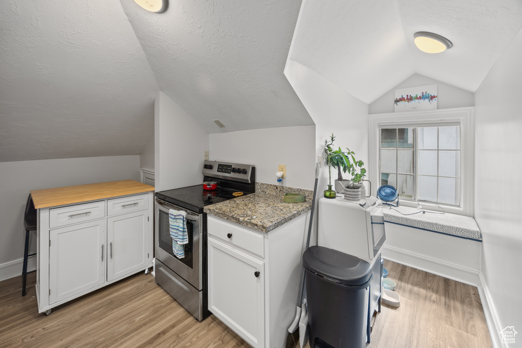 Kitchen featuring electric range, lofted ceiling, light wood-style flooring, white cabinetry, and a textured ceiling