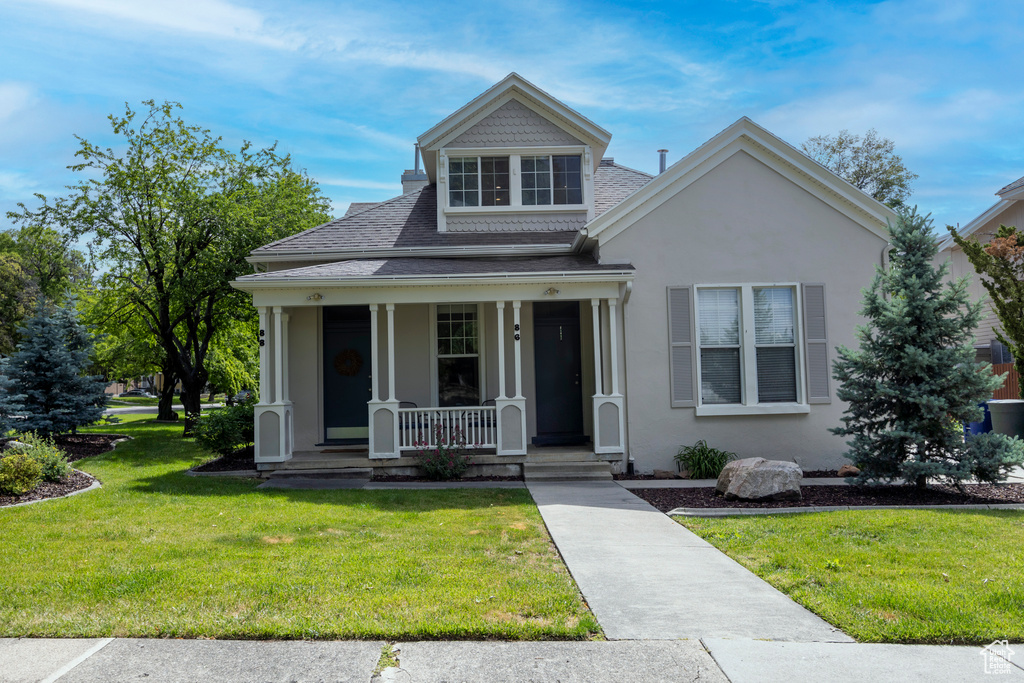 View of front of house featuring covered porch, a shingled roof, stucco siding, and a front lawn