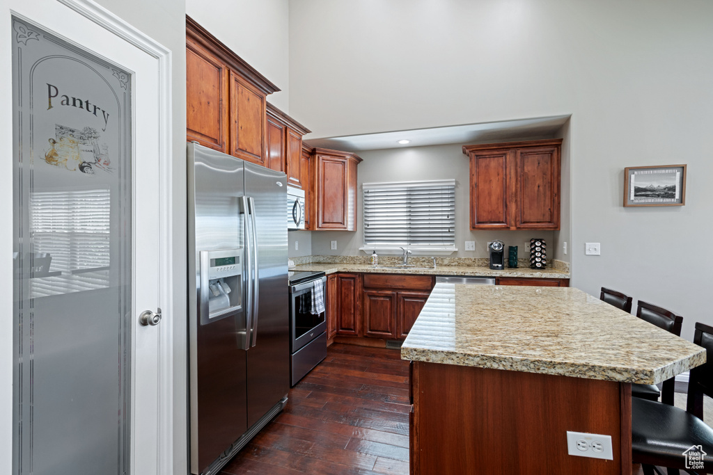 Kitchen with appliances with stainless steel finishes, a sink, a kitchen breakfast bar, dark wood finished floors, and a center island