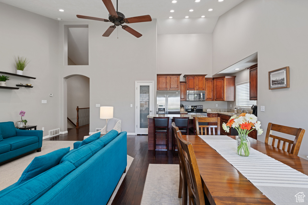 Dining room with a towering ceiling, arched walkways, a ceiling fan, recessed lighting, and dark wood finished floors