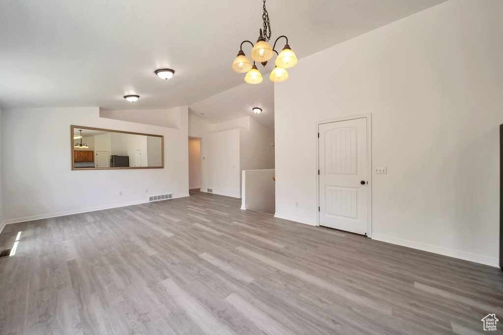 Unfurnished living room featuring wood finished floors, a chandelier, lofted ceiling, and baseboards
