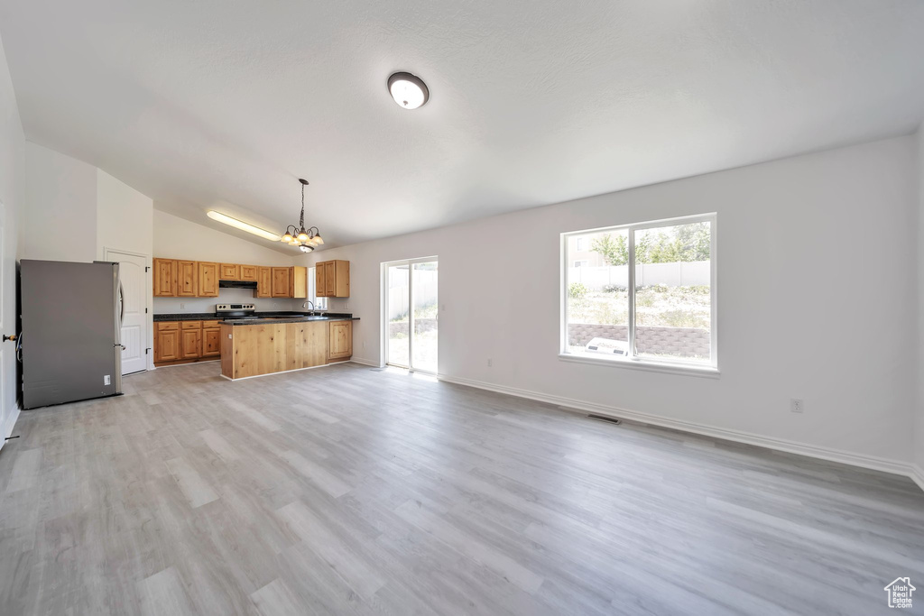 Unfurnished living room with a chandelier, lofted ceiling, plenty of natural light, light wood-style floors, and baseboards