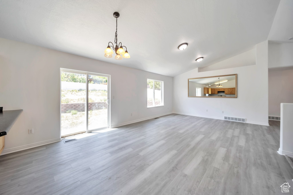Unfurnished living room with a chandelier, wood finished floors, lofted ceiling, and baseboards
