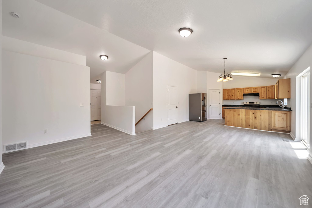 Unfurnished living room featuring vaulted ceiling, light wood-style flooring, a chandelier, and baseboards