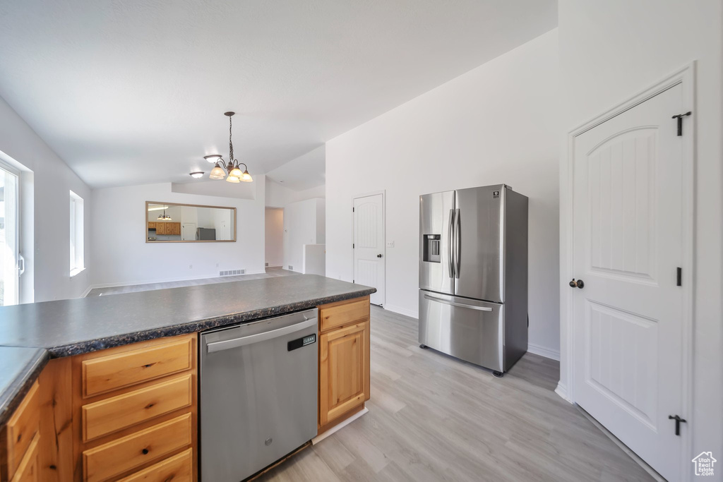 Kitchen with stainless steel appliances, vaulted ceiling, dark countertops, light wood-style flooring, and a chandelier