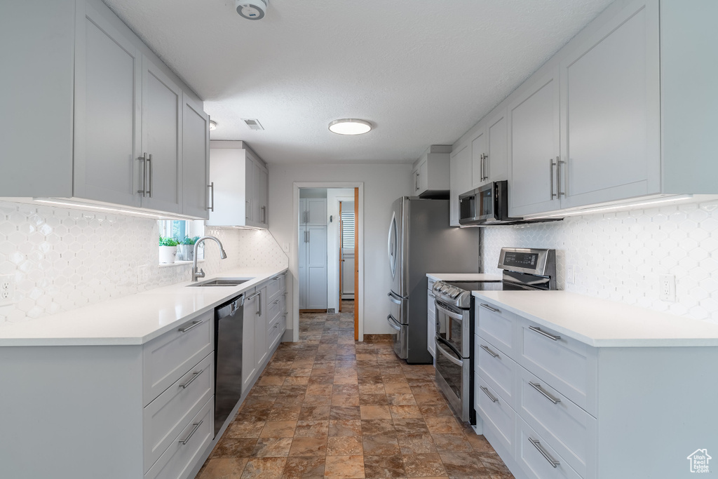 Kitchen with stainless steel appliances, a sink, stone finish floors, backsplash, and light countertops