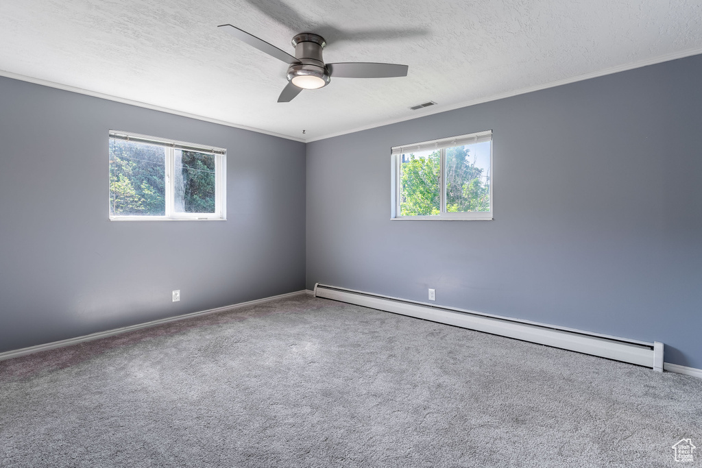 Carpeted spare room with baseboard heating, ceiling fan, crown molding, a textured ceiling, and baseboards