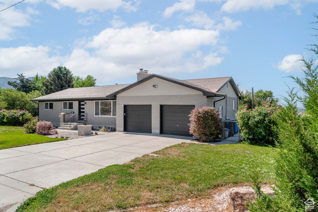 Single story home featuring a garage, concrete driveway, a front lawn, brick siding, and a chimney
