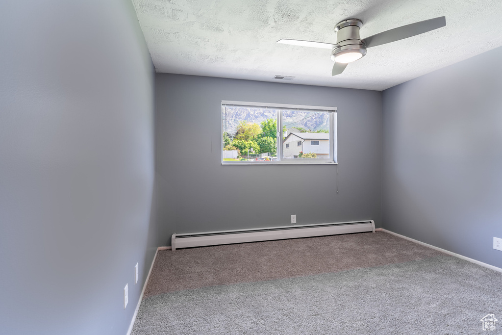 Spare room featuring a baseboard radiator, a textured ceiling, carpet, ceiling fan, and baseboards