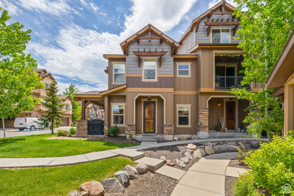 Craftsman house with a balcony, stone siding, board and batten siding, and a front lawn