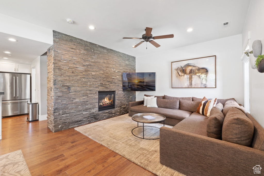 Living room with a ceiling fan, light wood-style floors, a stone fireplace, and recessed lighting